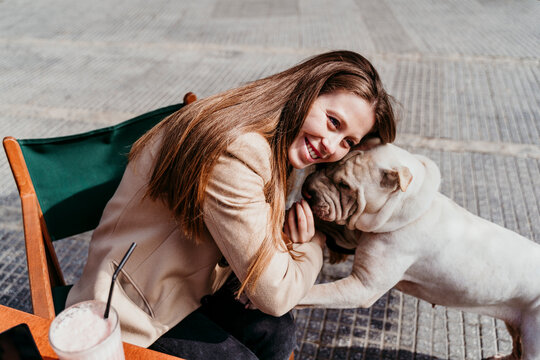 Smiling woman leaning on pet while sitting at sidewalk cafe