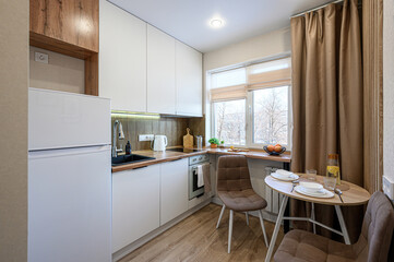 bright kitchen featuring white cabinets, wooden countertops, and a small dining area with brown chairs. Sunlight streams through the window, illuminating the cozy space