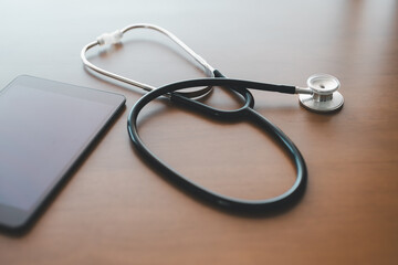 Fototapeta premium Modern healthcare concept featuring stethoscope and smartphone on wooden desk, symbolizing telemedicine, digital health services, and the integration of mobile technology in clinical medical practice.