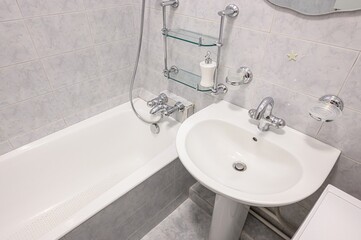 clean bathroom featuring a white bathtub, pedestal sink, and tiled walls. Chrome fixtures and glass...