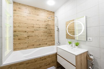 Modern bathroom featuring wood-look tiles, white fixtures, and a stylish, illuminated mirror above...