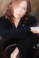 A female model poses sitting on a chair among nature and fields, an unusual photo of a summer Look