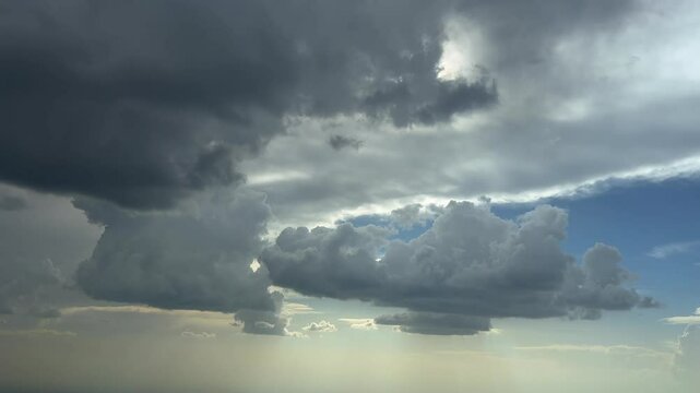 An aerial cloudscape recorded from a jet cockpit while flying through a stormy sky full of threatening storm clouds under a blue sky with a radiant sun above