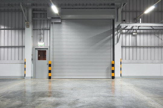 Concrete floor and shutter door inside industrial building at night. To construction for factory or warehouse. New clean and shiny surface. Nobody and empty space suit for product display background.
