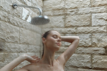 Relaxed woman under shower with natural stone wall background, enjoying warm water spray in a...