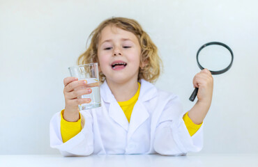 A child examines water with a magnifying glass. Selective focus.