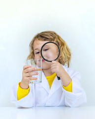 A child examines water with a magnifying glass. Selective focus.