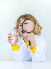 A child examines water with a magnifying glass. Selective focus.