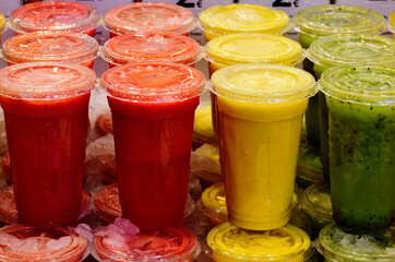 colorful fruit juice cups. transparent clear plastic with caps. shaved ice on top. street vendor stand. closeup view. healthy eating and essential vitamins. freshness concept. strawberry, peach, kiwi 