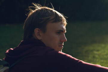 Young man gazing thoughtfully in sunlight on green grass