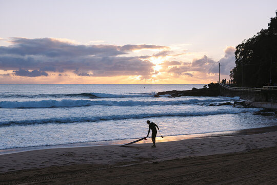 Surfer preparing surfboard on the beach at sunrise