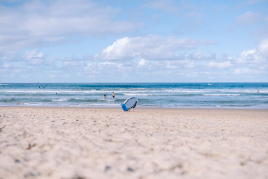Bodyboard standing on sandy beach with surfers in background