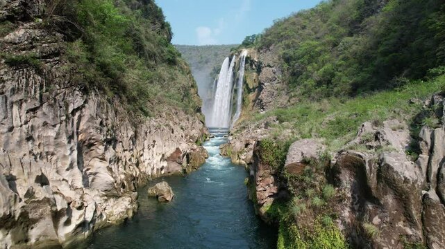 Drone flies toward the spectacular Tamul Waterfall in Mexico, where a rainbow forms in the mist above the cascading water, revealing a breathtaking natural landscape.