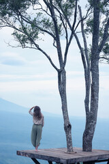 A girl is meditating, standing on a platform in the mountains, against the backdrop of a landscape...