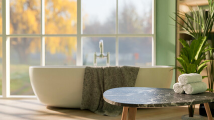 Black marble stool table with towels and white ceramic bathtub near glass wall with garden view.