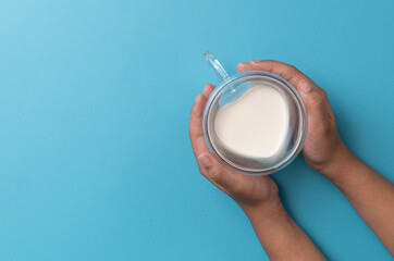 Hand holding a heart-shaped glass with milk sits against a blue background
