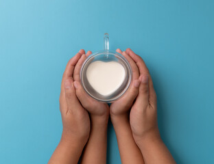 Hand holding a heart-shaped glass with milk sits against a blue background