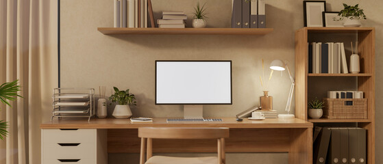 Blank screen computer on wooden table and a chair under hanging display shelf in a cosy study room.