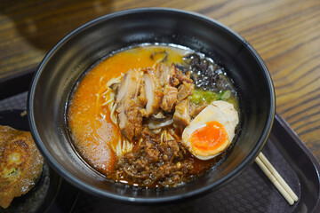 Spicy Chicken Ramen with Egg in Black Bowl on Wooden Table