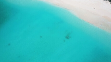 Aerial view capturing a pristine white sand beach seamlessly merging with crystal-clear turquoise water, creating an idyllic tropical paradise perfect for relaxation and tranquility