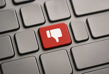 Red keyboard key with a thumbs-down icon among grey keys, representing digital disapproval, criticism or social media rejection in a tech environment.
