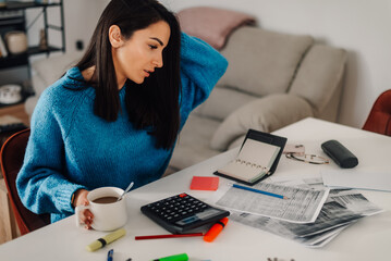 Stressed young woman managing home finances and calculating bills at table