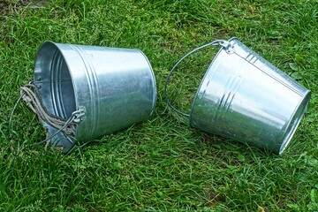 two iron simple empty clean industrial new shiny with handles garden round buckets lie on green...