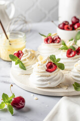 Meringues mini pavlova cakes with whipped cream decorated with fresh cherry berries and mint leaves on white marble background. Light summer dessert