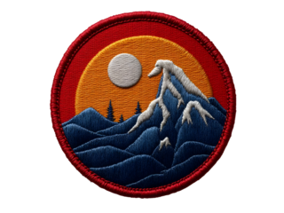 Circular embroidered patch with red border, blue mountains, orange sky, pine tree silhouettes and textured stitching PNG file isolated on transparent background
