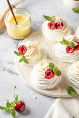 Meringues mini pavlova cakes with whipped cream decorated with fresh cherry berries and mint leaves on white marble background. Light summer dessert