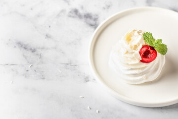 Meringues mini pavlova cake with whipped cream, fresh cherry and mint leaves on a plate, white marble background. Light summer dessert, copy space