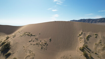 Hikers walking along the crest of a large sand dune in a serene desert landscape, soaking in the vastness and tranquility of nature's stunning beauty
