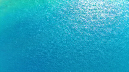 Aerial view capturing a vast turquoise expanse of gently rippling water under bright sunlight, creating a tranquil and idyllic tropical paradise