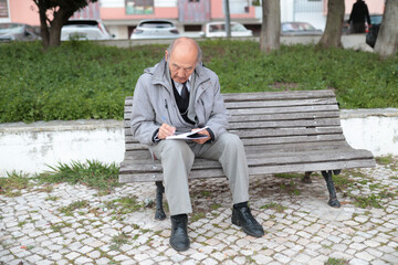Senior professor writing notes sitting on bench in university campus park