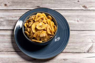 Dried banana slices arranged in a blue bowl placed on a wooden surface. A natural and healthy snack in a rustic setting. Healthy eating