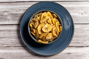 Dried banana slices arranged in a blue bowl placed on a wooden surface, A natural and healthy snack in a rustic setting.healthy food