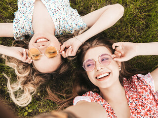 Two young beautiful smiling hipster female in trendy summer sundress.Sexy carefree women lying on...