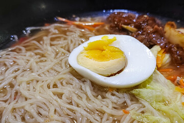 A bowl of noodle soup topped with half a boiled egg, vegetables, and meat.