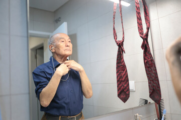 Senior man adjusting his shirt collar in bathroom mirror