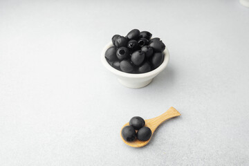 Black olives in white bowl and wooden spoon on bright background