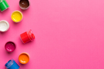 jars with gouache of different colors on Colored background. hobby painting. Top view with empty...