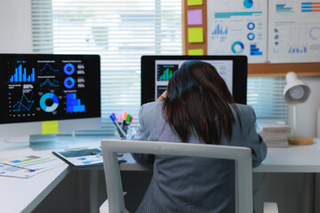 Stressed businesswoman sleeping at office desk with charts on computer screens