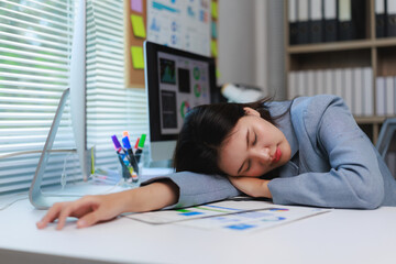 Exhausted asian businesswoman sleeping at her desk after working late