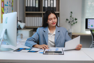 Asian businesswoman analyzing charts and documents at office desk