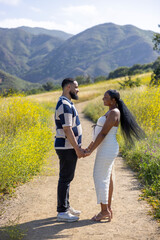 A joyful and expectant couple stands together outdoors, surrounded by lush greenery and majestic mountains, celebrating their exciting journey into parenthood, filled with love and anticipation