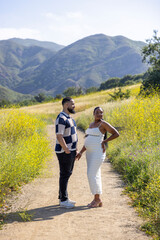 An African American couple enjoys a warm summer day outdoors, celebrating their pregnancy journey amidst scenic mountains and blooming flowers, creating lasting memories filled with love