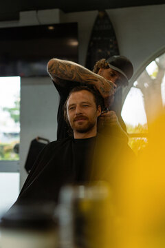 Tattooed barber trims smiling man's hair in modern barbershop