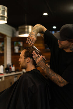 Tattooed barber giving precise haircut to male client