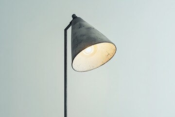 A close up view of a gray metal lamp with a bright lightbulb against a plain light background wall