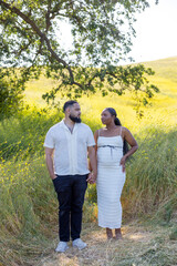 On a bright, sunny summer day, an African American couple joyfully celebrates their beautiful journey into parenthood, surrounded by lush greenery and the stunning beauty of nature all around them